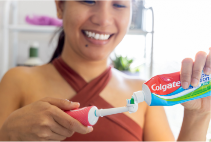 Woman smiling while adding Colgate toothpaste to a toothbrush in a bathroom.